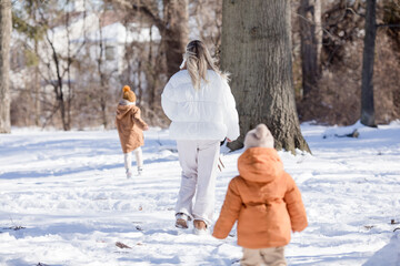 An active and happy mother walks along a path in the winter forest together with her little sons. Winter family holidays. Happy motherhood.
