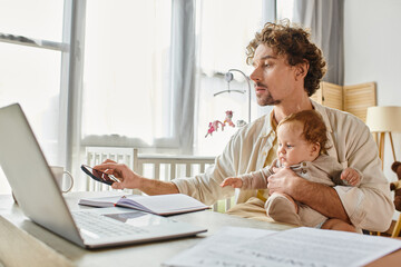 father holding his baby son while taking his smartphone and working from home, work-life balance
