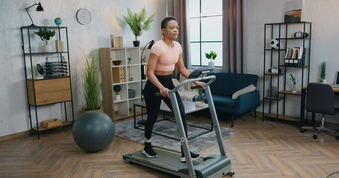 African American woman in sportswear doing walking exercises on treadmill during morning home workout
