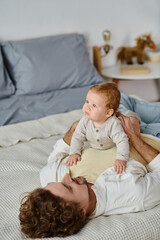 man with curly hair and beard hugging his infant son on a bed, bonding between father and child