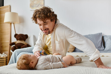 cheerful single father giving pacifier to his infant baby son on the bed, fatherhood and love