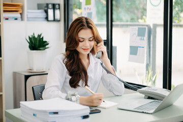 Business asian woman Talking on the phone and using a laptop with a smile while sitting at office.