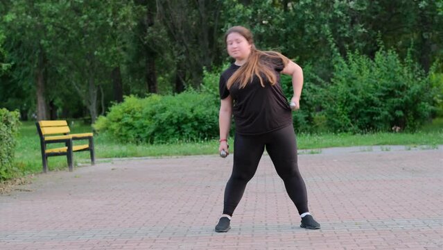 Overweight girl doing sports outdoors, lifting dumbbells