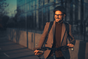 A happy young businessman in a brown suit pushing his bicycle on his way home and admiring the...
