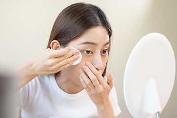 Skin care routine concept, Woman looking in the mirror and using cotton pad and toner to remove...