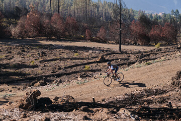 Male cyclist riding a gravel bicycle a gravel road through burned forest on Tenerife, Canary Islands, Spain. Sport motivation. Cycling training outdoors in Spain. Cycling adventure .