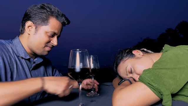 Drunk Man burble gabble or Mumbling as woman sleeps at dinner table with wine glasses on the beach at night