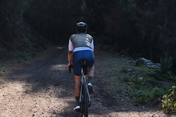 Fototapeta premium Close up back view of male cyclist riding a gravel bicycle a gravel road in forest on Tenerife, Canary Islands, Spain. Sport motivation. Cycling training outdoors in Spain. Cycling adventure .