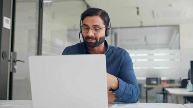 Busy Indian call center agent wearing headset talking to client working in customer support office. Professional contract service operator telemarketing representative using laptop having conversation
