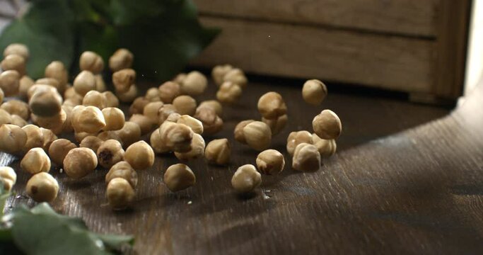 Super slow motion macro of fresh bio organic peeled dried hazelnuts are falling on wooden rustic table in kitchen of restaurant at 1000 fps.