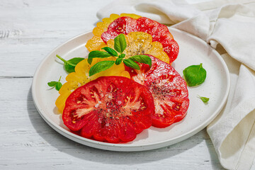 Colorful Heirloom tomato harvest. Ripe ribbed vegetables with fresh basil leaves. Wooden background
