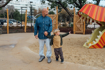 Father and son on the playground in sunny day. Both dad and child are smiling. Family fun outdoor and father and son spend time together.