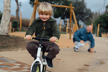 Dad teaches his son riding on bicycle in park. Father and son smile and have fun together