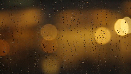 Blurred shot of raindrops on a glass surface with shimmering light.