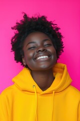 A woman wearing a yellow hoodie smiles directly at the camera. This image can be used to depict happiness, positivity, or casual fashion