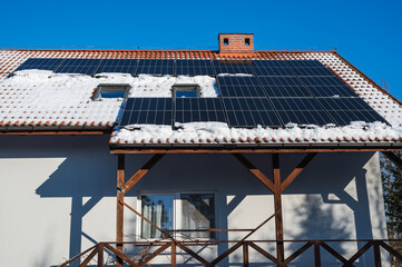 Photovoltaic panels on the roof of the house covered partly by snow.