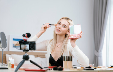 Fototapeta na wymiar Young woman making beauty and cosmetic tutorial video content for social media. Beauty blogger smiles to camera while showing how to beauty care to audience or followers. Blithe