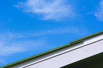 Green roof gable on blue sky and cloud background.