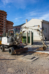 Excavator with a jackhammer against the background of city houses
