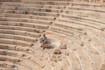 Tourist man sitting on the steps of The ancient Greek amphitheater at the ancient City in Antalya...