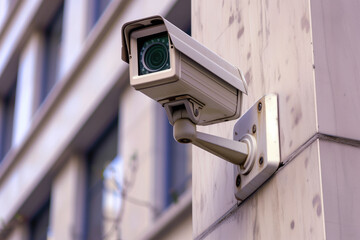 Through the lens of a camera mounted on a wall, a bustling street scene is captured with the building's windows reflecting the vibrant outdoor energy