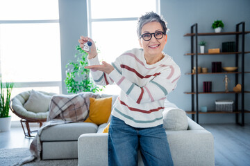 Photo of positive friendly grandmother hand hold demonstrate new house key spacious interior indoors