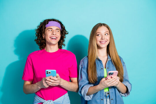 Photo of young two teenage girlfriend with boyfriend tricky looking each other sending memes using phones isolated on cyan color background