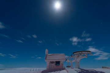 View of the starry sky in winter, at the top of the mountain, the building and the cable car are covered with snow.