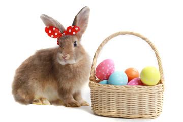 Fototapeta na wymiar Cute fluffy brown rabbit with long ears wearing red bow and colorful easter eggs basket on white background, bunny animal with easter egg, symbol of happy easter holiday festival. Spring celebration.