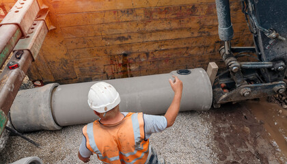 Builder installing big diameter concrete drainage pipe protected by trench support system during...