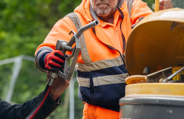 Builder in safety gloves filling excavator with diesel fuel on building site