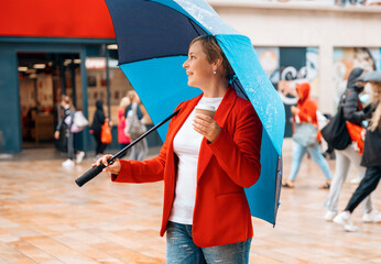a woman in a red jacket with coffee under an umbrella walking around a modern city