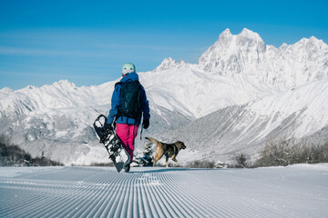 Female snowboarder walking with dog on Snow trail from ratrak preparation, freshly groomed ski...