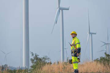 male engineer standing against turbines on wind turbine farm.