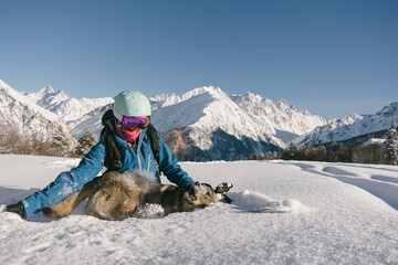Female snowboarder freerider  hiking with dog on ski resort, winter sport outdoor, sunny day in mountains