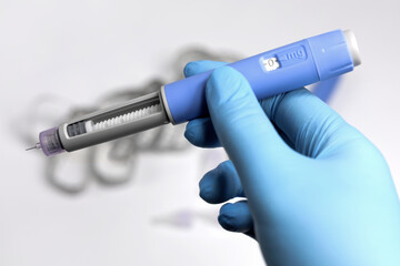 Hands in surgical gloves holding Ozempic Insulin injection pen for diabetics.