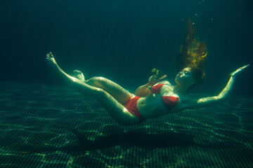 A beautiful red-haired woman poses with a cocktail under water.