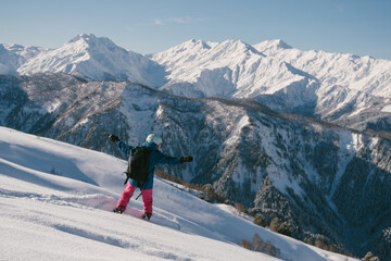 Fototapeta na wymiar female snowboarder riding on slope of powdery snow in high mountains. Freeride at ski resort, amazing mountain peaks skyline