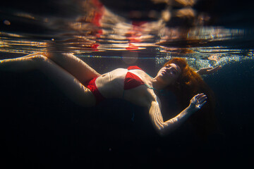 A beautiful sporty girl poses underwater with loose hair against the bright rays of the sun from...