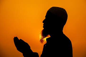 Asian Muslim bearded man praying with hands raised to God on sunset background. Silhouette of an old age Muslim praying during sunset.