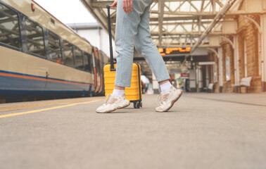 Obraz premium Traveler with a yellow suitcase waiting for a train at the train station on the platform. Travel concept.