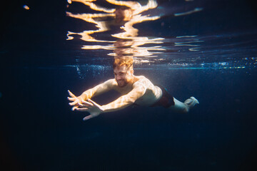 A handsome young man swims underwater in a swimming pool while on vacation.