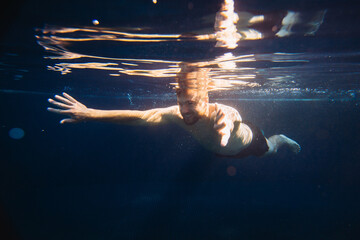 A handsome young man swims underwater in a swimming pool while on vacation.