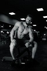 Fototapeta na wymiar Muscular man is sitting on chair in the gym.