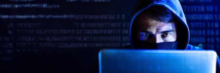 Hacker using laptop computer in dark room, cyber crime concept.