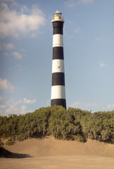 Black and white Lighthouse in Claromeco, with tamarix plants in the sand dunes and blue sky.