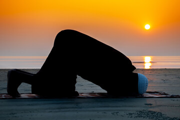 Asian Muslim man praying under the open sky by the sea at sunset. Silhouette of an old age Muslim praying during sunset.