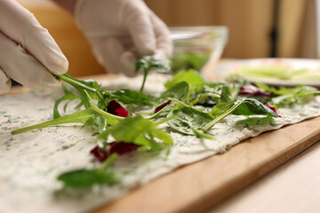 Greens are added to pita bread with cheese. Preparation of a roll with cheese, fish and vegetables