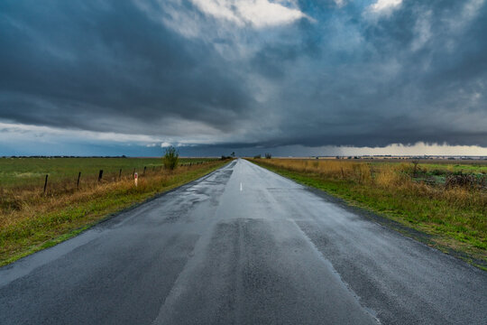 Rain falling from a dramatic stormfront over a long straight country road