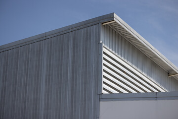 metal sheet factory warehouse against blue sky background. silver corrugated steel industrial roof.